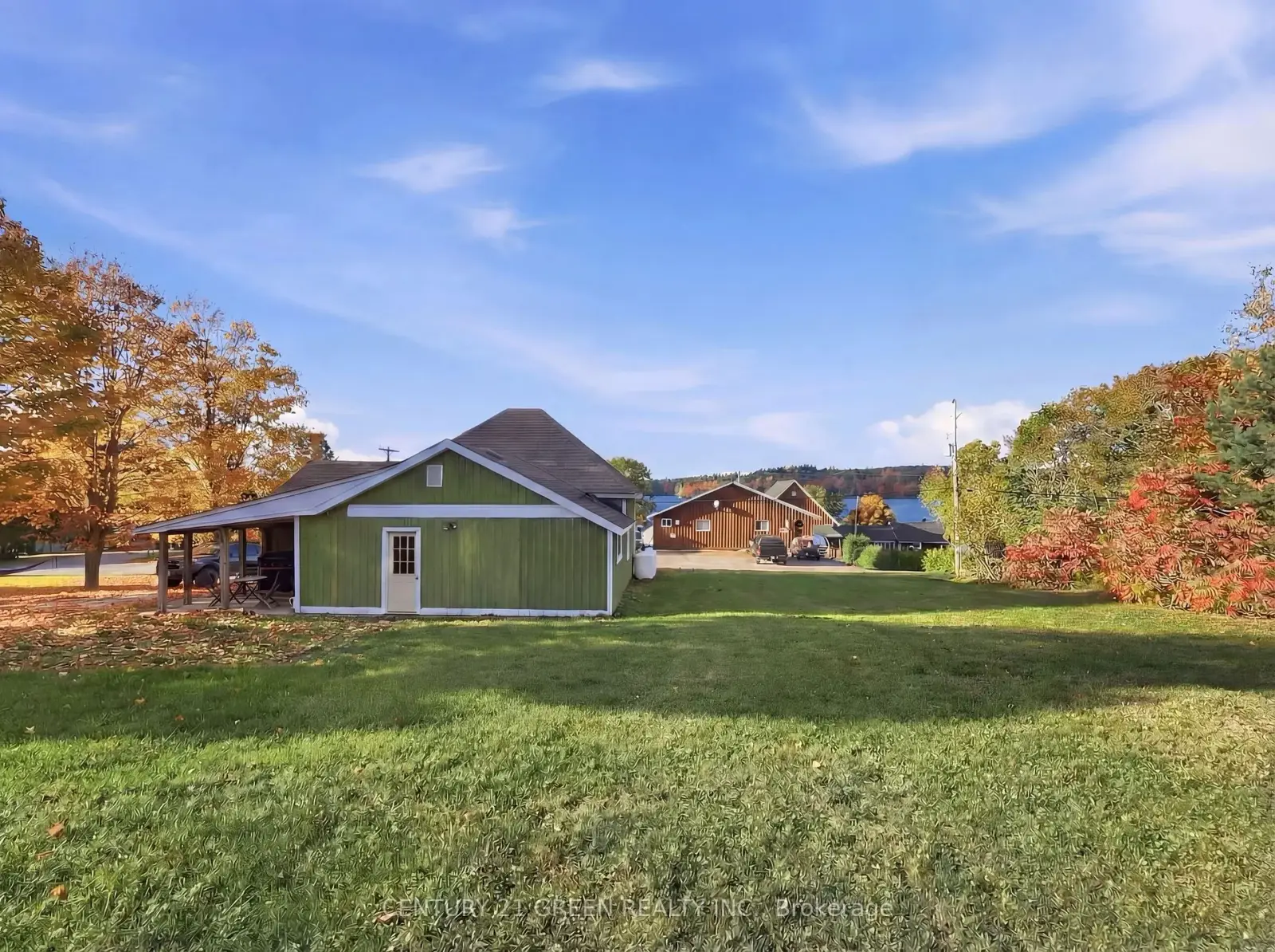 135 Village Street, Hastings Highlands — green bungalow with covered porch, broad lawn, autumn trees and a partial lake view