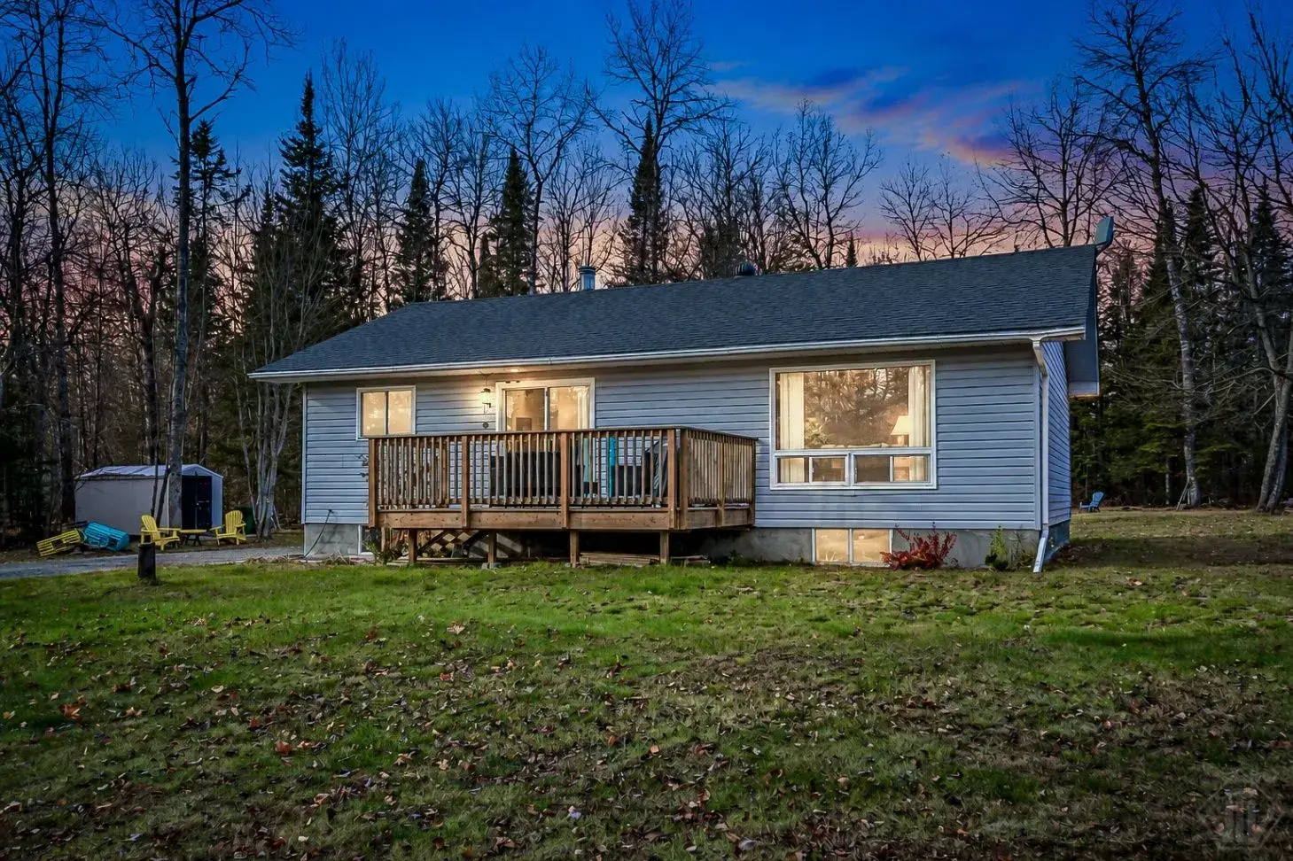 266 Bay Lake Road, Perry — rear exterior of the bungalow and wood deck at dusk, with mature trees behind the home